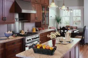 A modern kitchen with dark wood cabinets, marble countertops, stainless steel appliances, and a central island with a basket of fruit and a vase of white flowers.