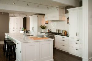 Modern kitchen with white cabinets, a large marble island with three black stools, stainless steel appliances, and wooden flooring.