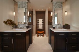 Modern bathroom with double sinks, dark wood cabinets, mosaic tile accents, two pendant lights, a walk-in shower, towel warmer, and decorative plants on each countertop.