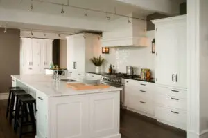 Modern kitchen with white cabinets, a large marble island with three black stools, stainless steel appliances, and wooden flooring.