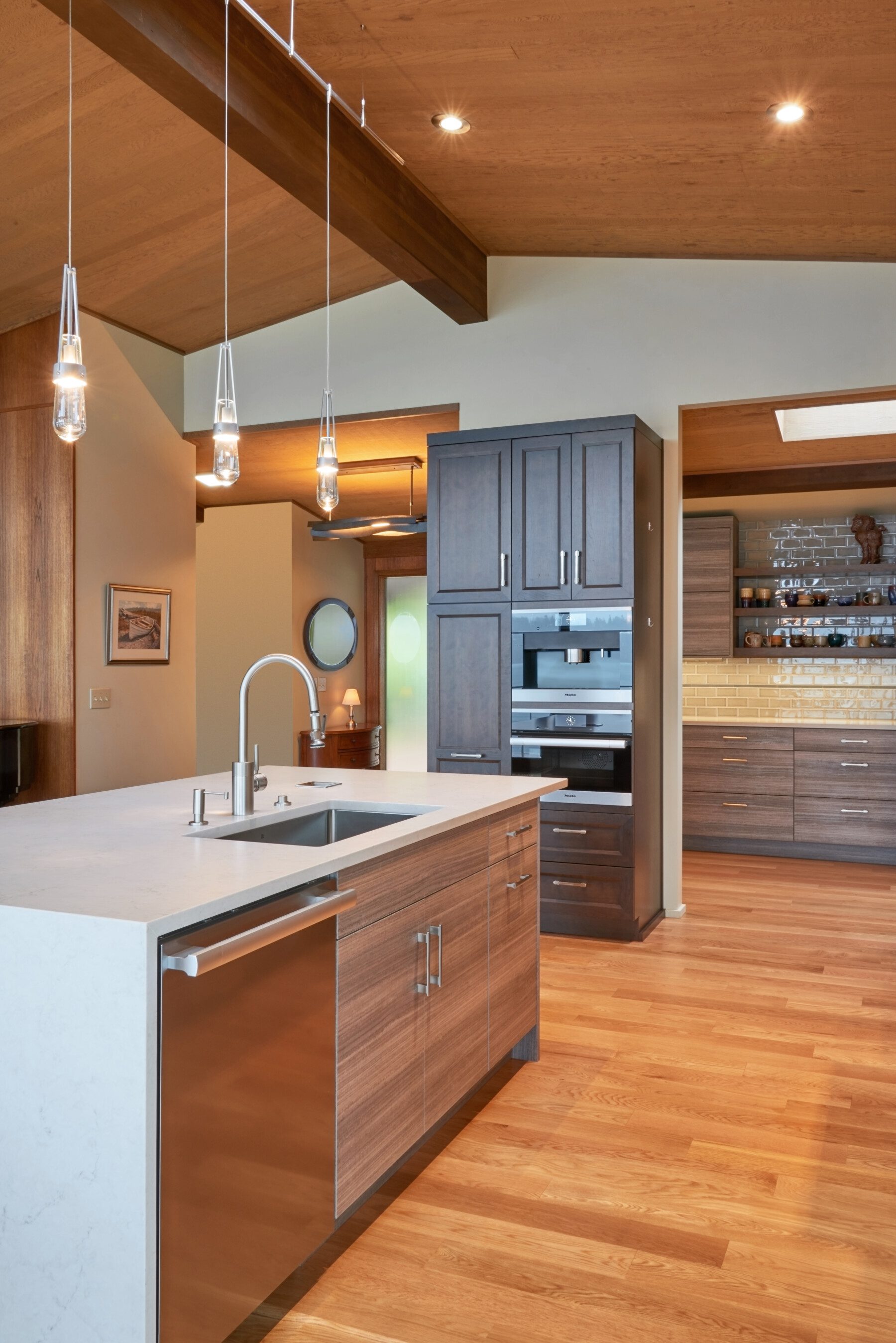 Modern kitchen with wood floors, island sink, stainless steel appliances, hanging pendant lights, and built-in cabinets.