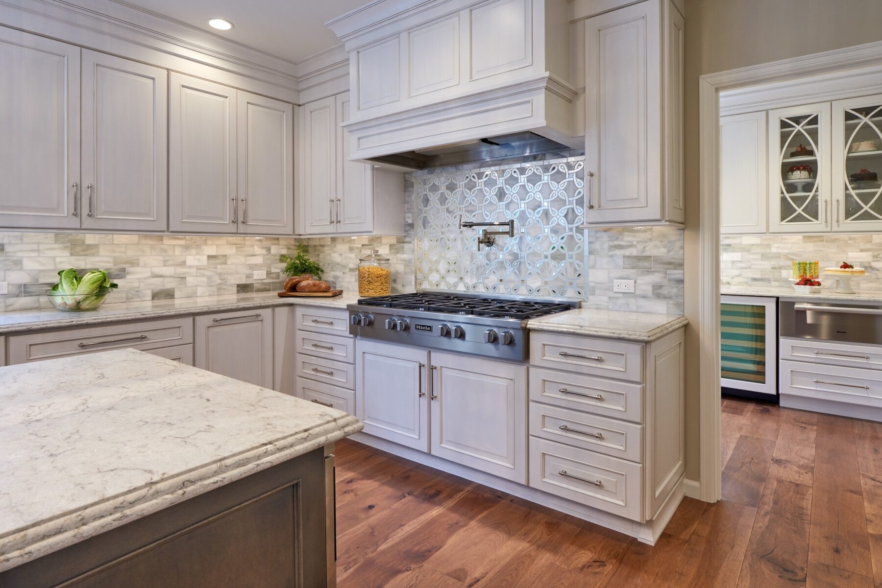 Modern kitchen with white cabinetry, marble countertops, stainless steel appliances, patterned backsplash, and wood flooring.