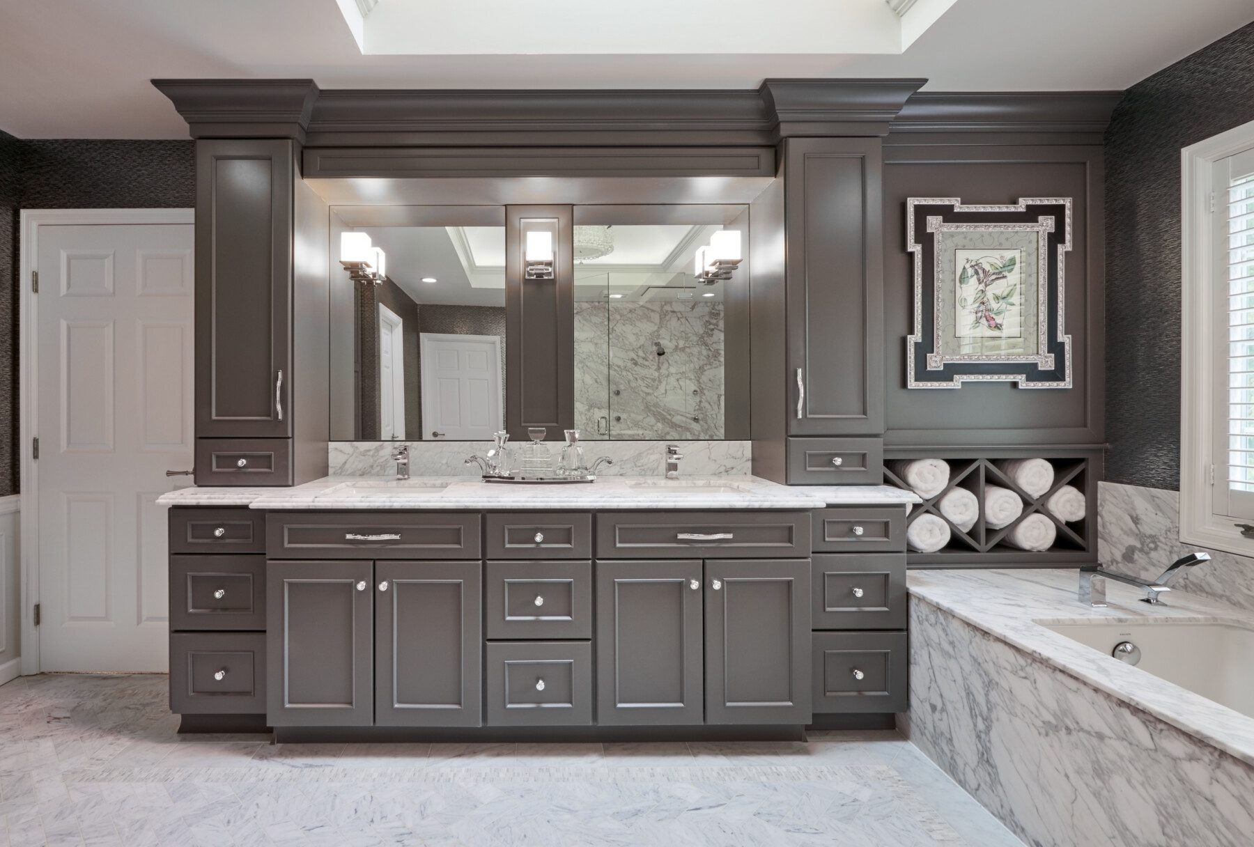 Modern bathroom with double sink vanity, marble countertop, rolled towels, built-in bathtub, wall art, and large mirror with sconces.
