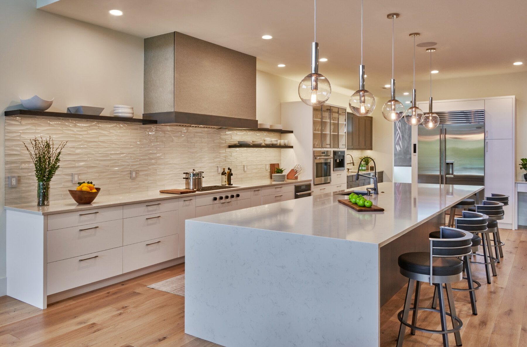 Modern kitchen with white cabinetry, large marble island with barstools, stainless steel appliances, pendant lights, and wood flooring.