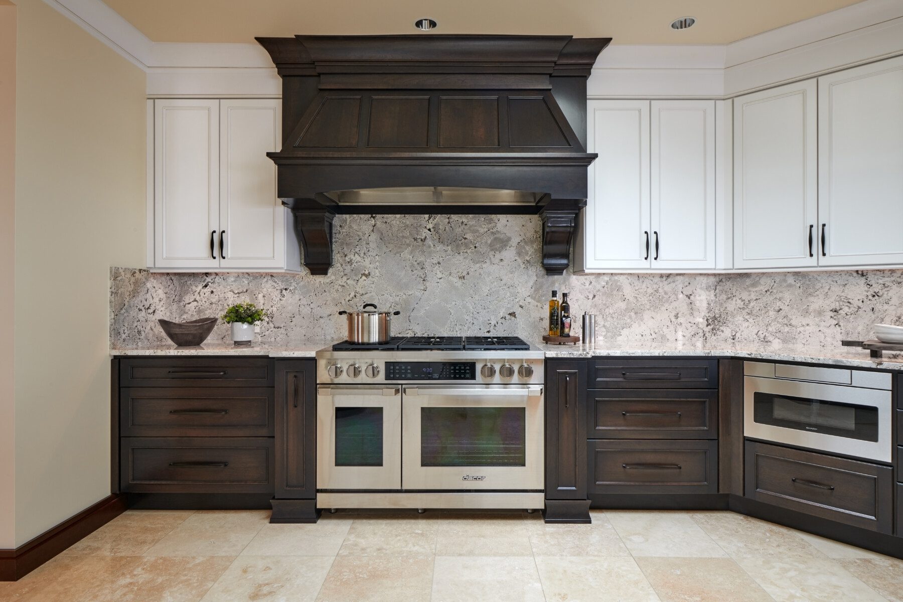Modern kitchen with a large stainless steel stove, dark wood cabinets, white upper cabinets, and a stone backsplash.