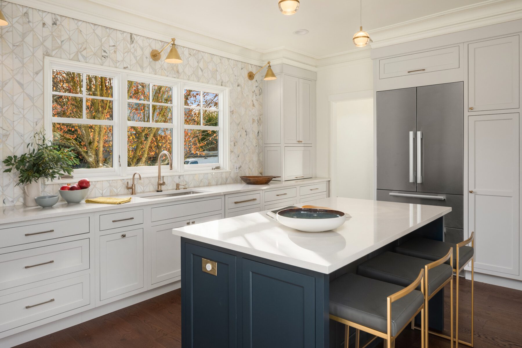 Modern kitchen with white cabinets, a large island with seating, stainless steel appliances, and a window above the sink letting in natural light.