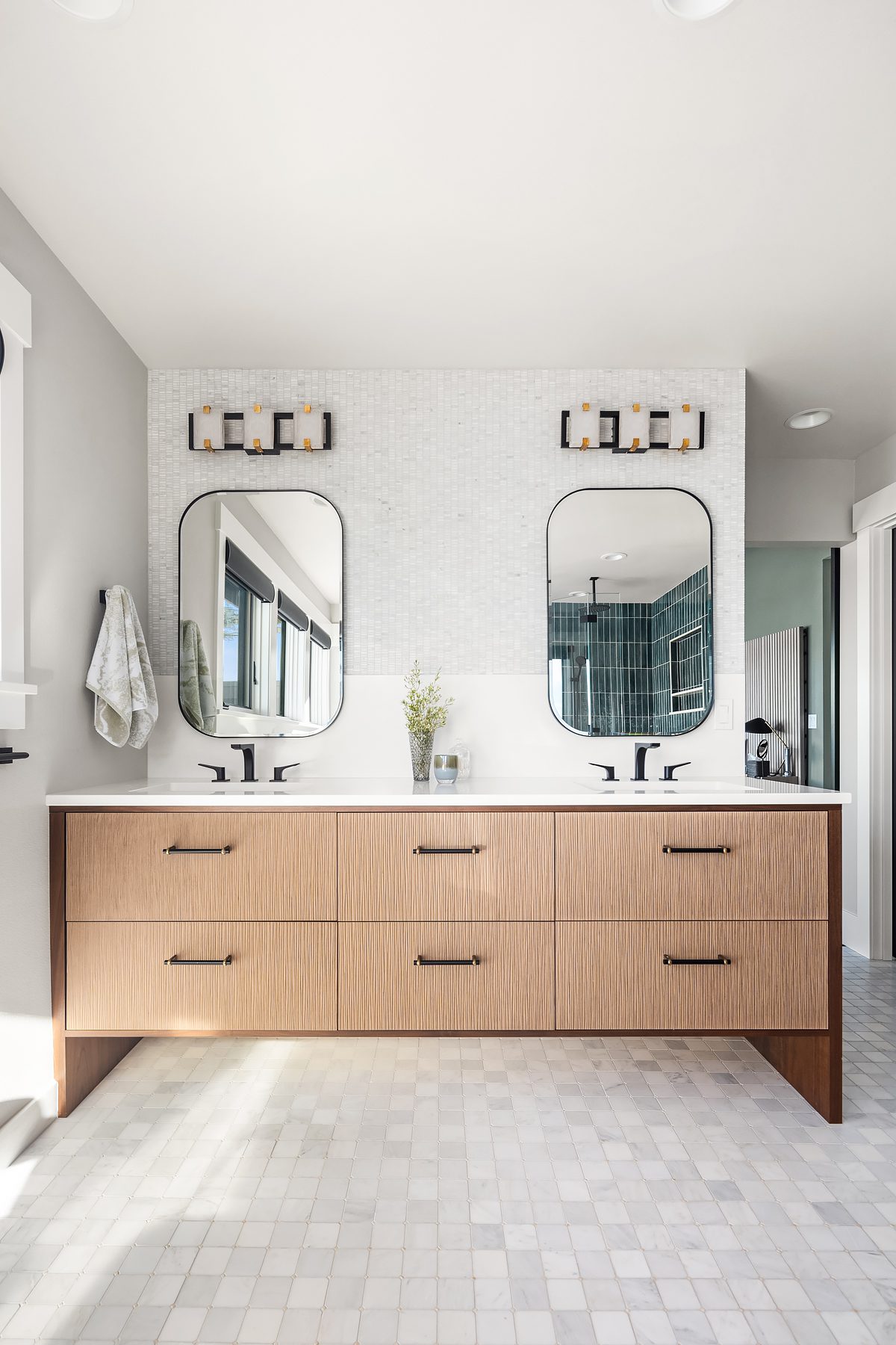 Modern bathroom with a double vanity, two rectangular mirrors, black fixtures, light wood cabinets, and a white tile backsplash.