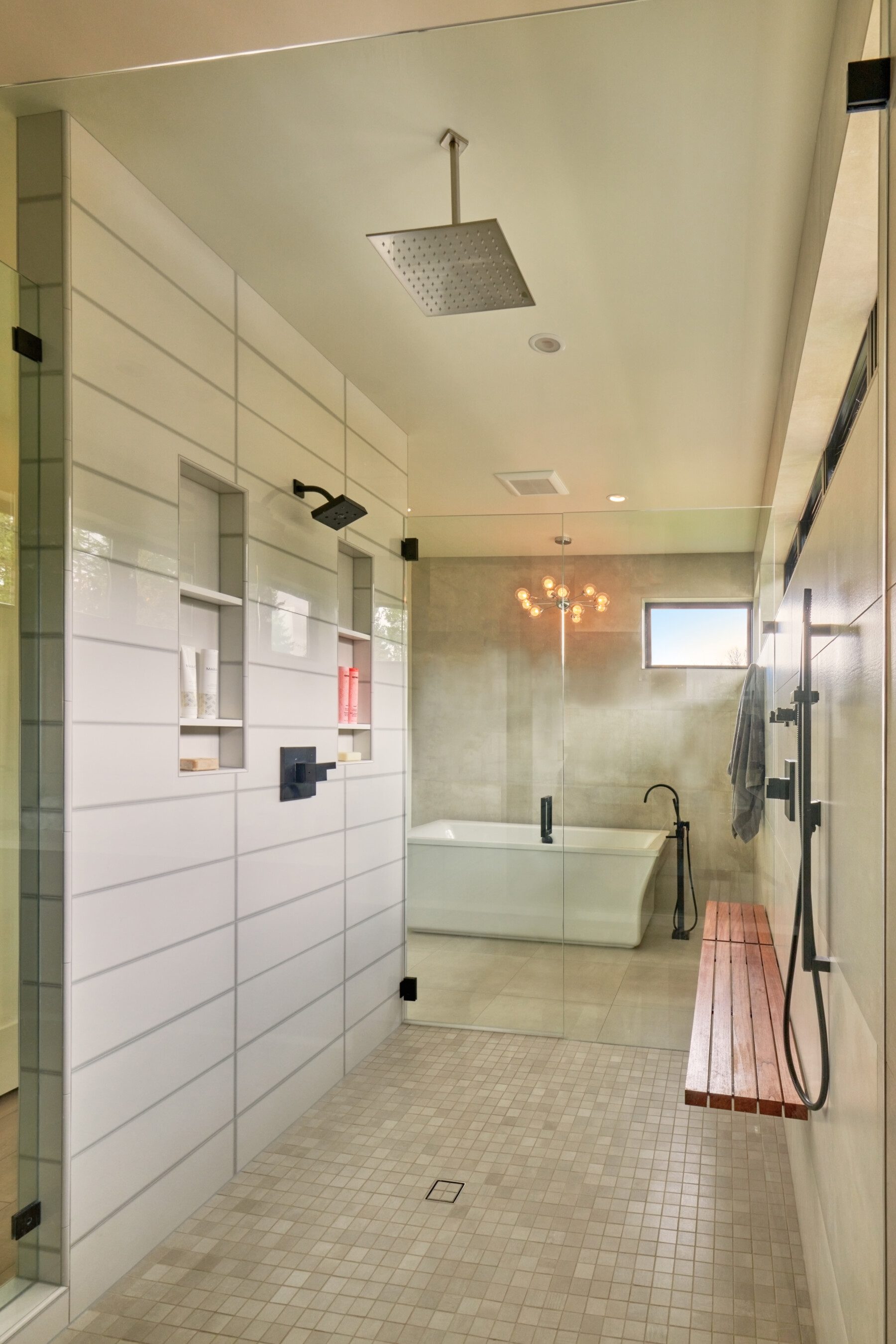 Modern bathroom with a walk-in shower, rainfall showerhead, wooden bench, glass partition, built-in shelves, freestanding bathtub, and a small window.