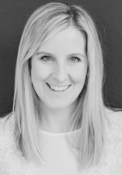 A woman with straight, shoulder-length light hair smiles at the camera. She is wearing a light-colored top and is posed against a dark background.
